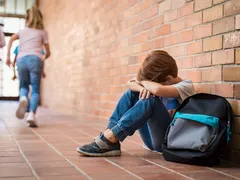 A young person sitting alone in a school hallway