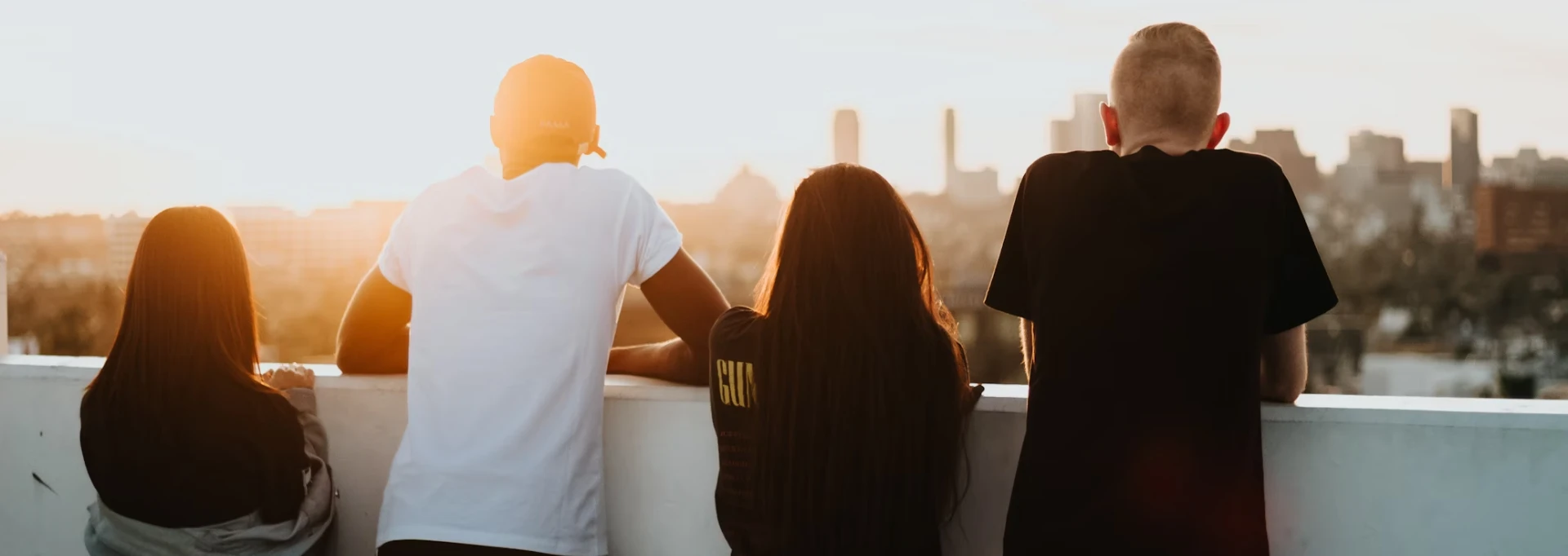 Four people sit on a ledge, facing a city skyline during sunset, highlighted by warm sunlight as part of the Yo Girl Youth Initiative.