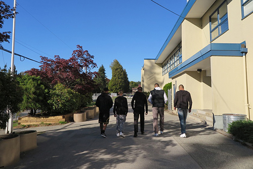 Four men walking on a sidewalk next to a building, with trees and a clear blue sky in the background, symbolizing potential resources for urban planning.