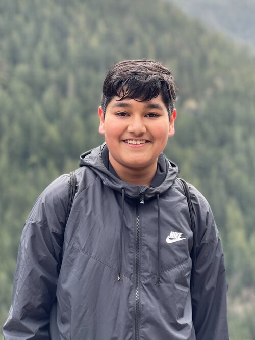 Young person with a black jacket smiling in front of a blurred green mountainous background, ready to explore our services.