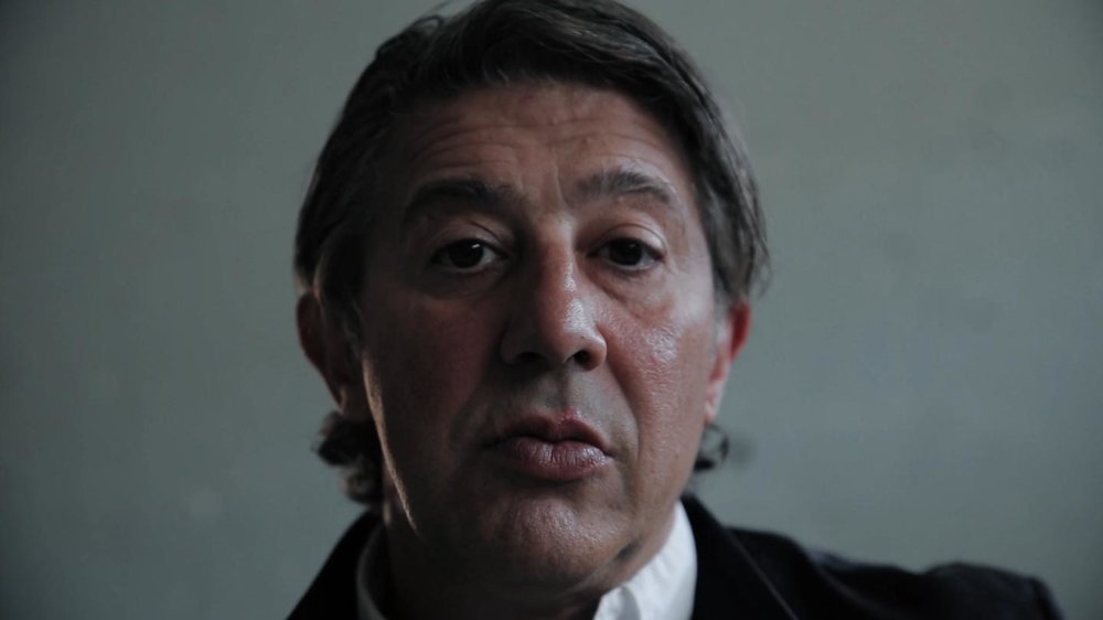 Close-up of an ex-Hells Angel, a middle-aged man with a serious expression, looking directly at the camera, grey background.
