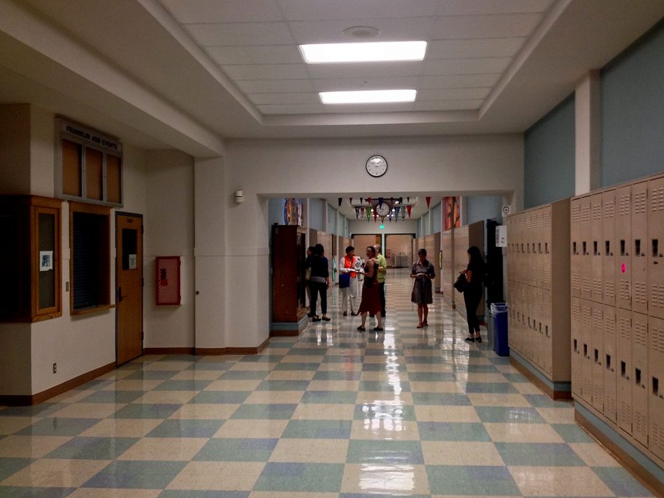 Students and teachers in a school hallway with lockers on the side, a clock on the wall, and tiled flooring steer youth away from lives of crime.