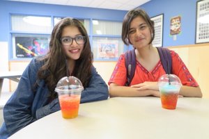 Two teenagers sitting at a table with colorful slush drinks, smiling in a bright indoor setting, participating in one of our engaging youth programs.